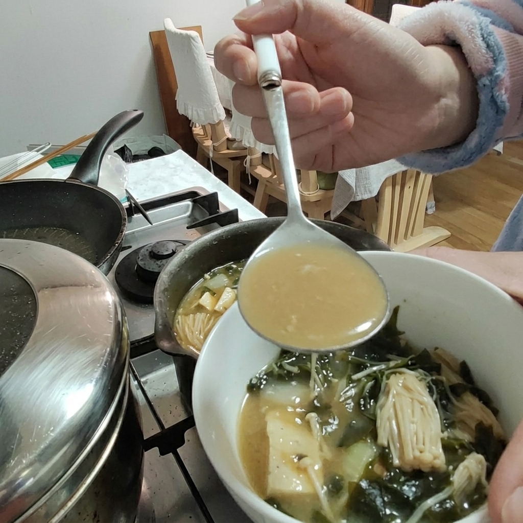 Pasta sojowa dodawana do gulaszu za pomocą chochli, widoczne tofu i grzyby enoki.