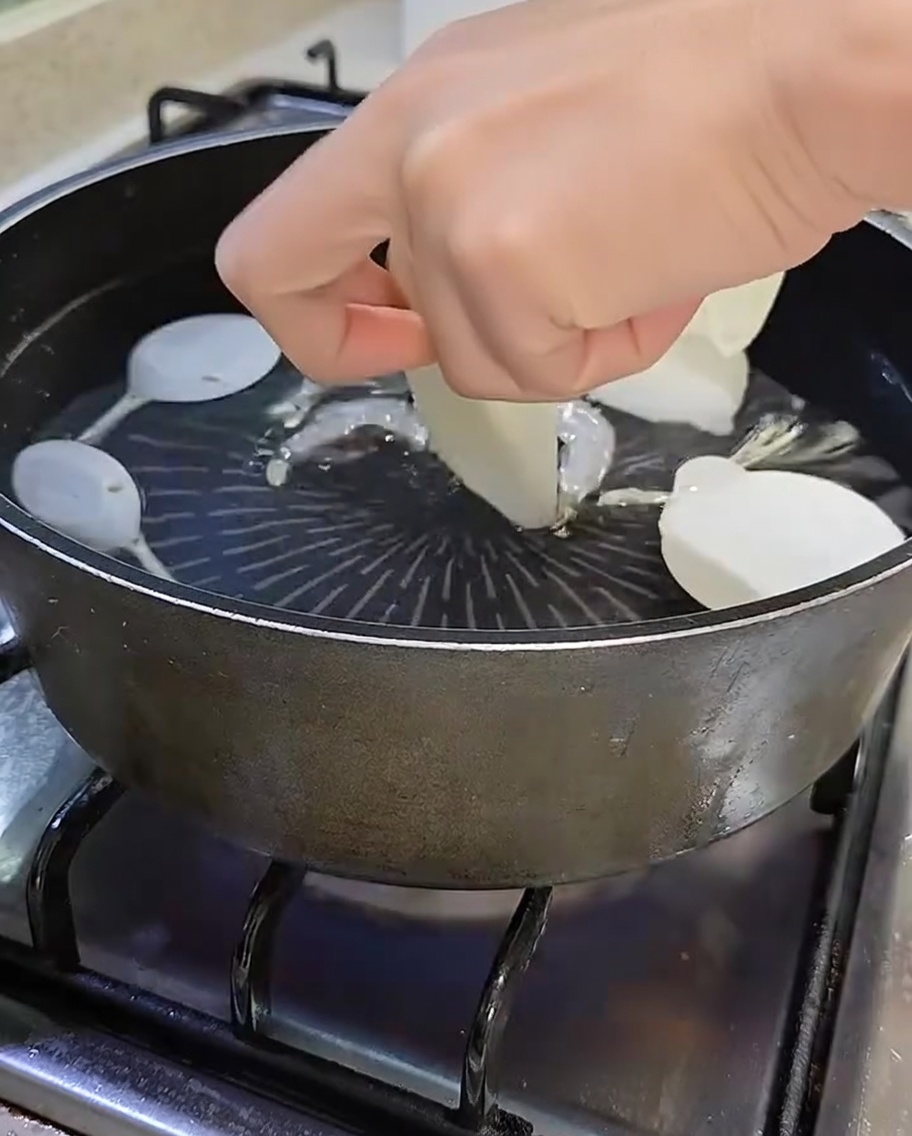 Garnek z gotującą się wodą, anchois, shiitake, plasterkami rzodkwi i zielonym szczypiorkiem.