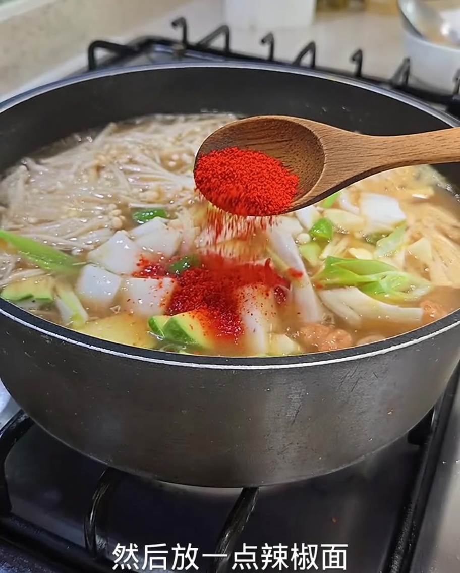 Zbliżenie na czerwone chili w proszku sypane z drewnianej łyżki do gotującego się gulaszu.