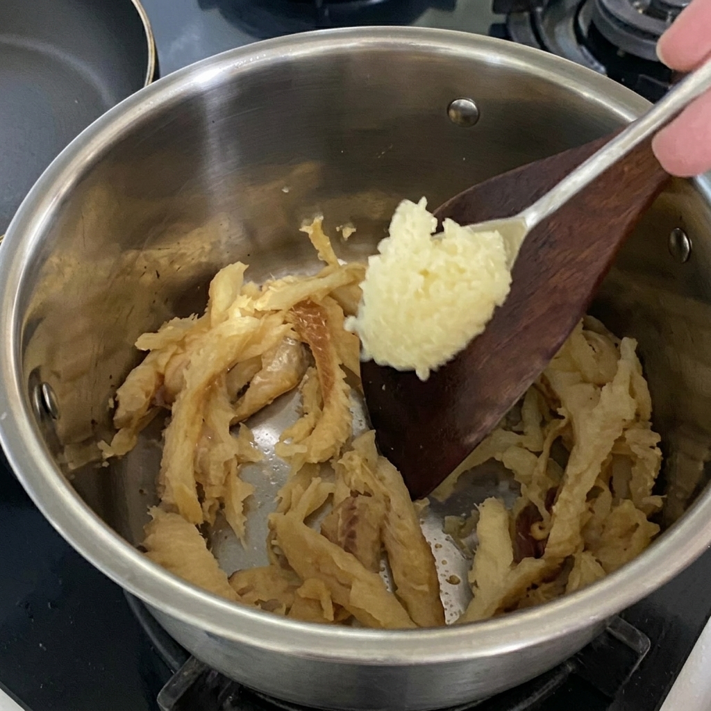 Łyżka posiekanego czosnku dodawana do smażonego mintaja w garnku.