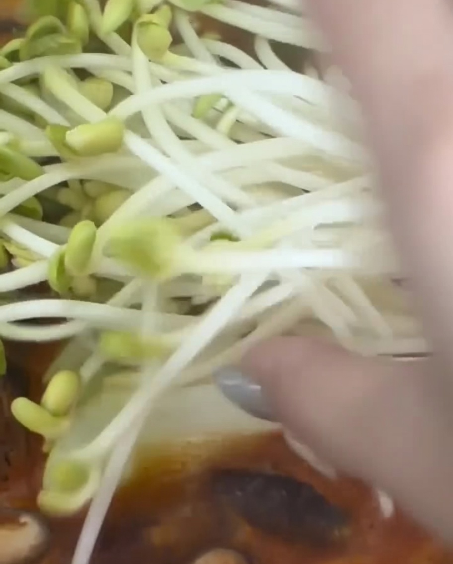 Garść świeżych kiełków soi dodawana do gotującego się koreańskiego gulaszu.