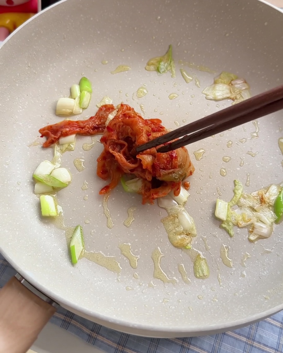 Kimchi mieszane na patelni z podsmażoną zieloną cebulką.