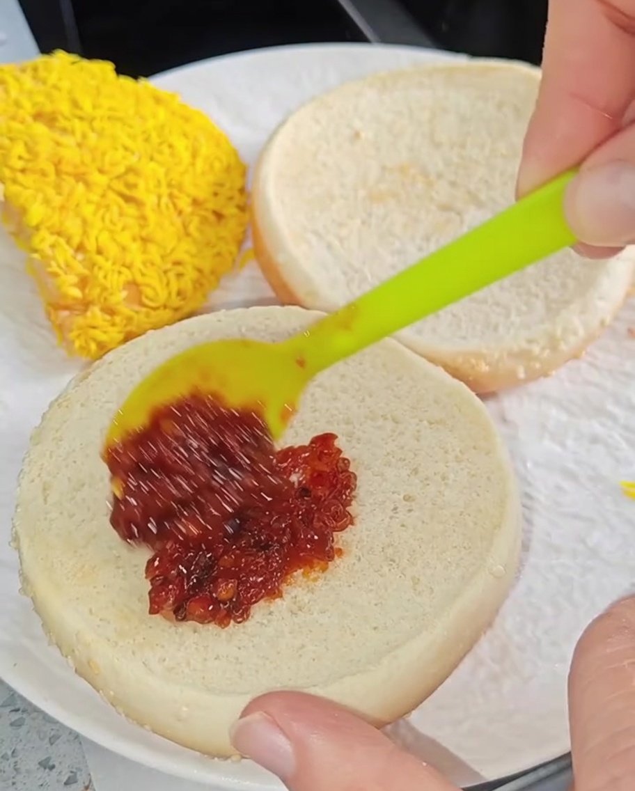 Mała szpatułka rozprowadzająca czerwony sos chili na wewnętrznej stronie podpieczonej bułki do burgera.