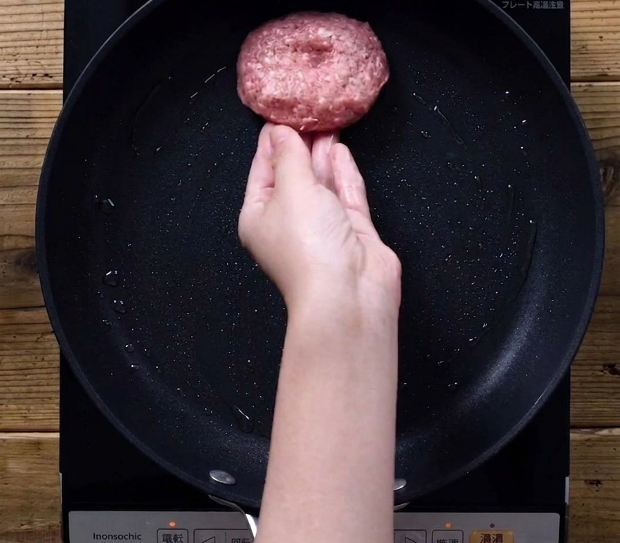 Dłoń kładzie surowy kotlet na rozgrzaną patelnię.