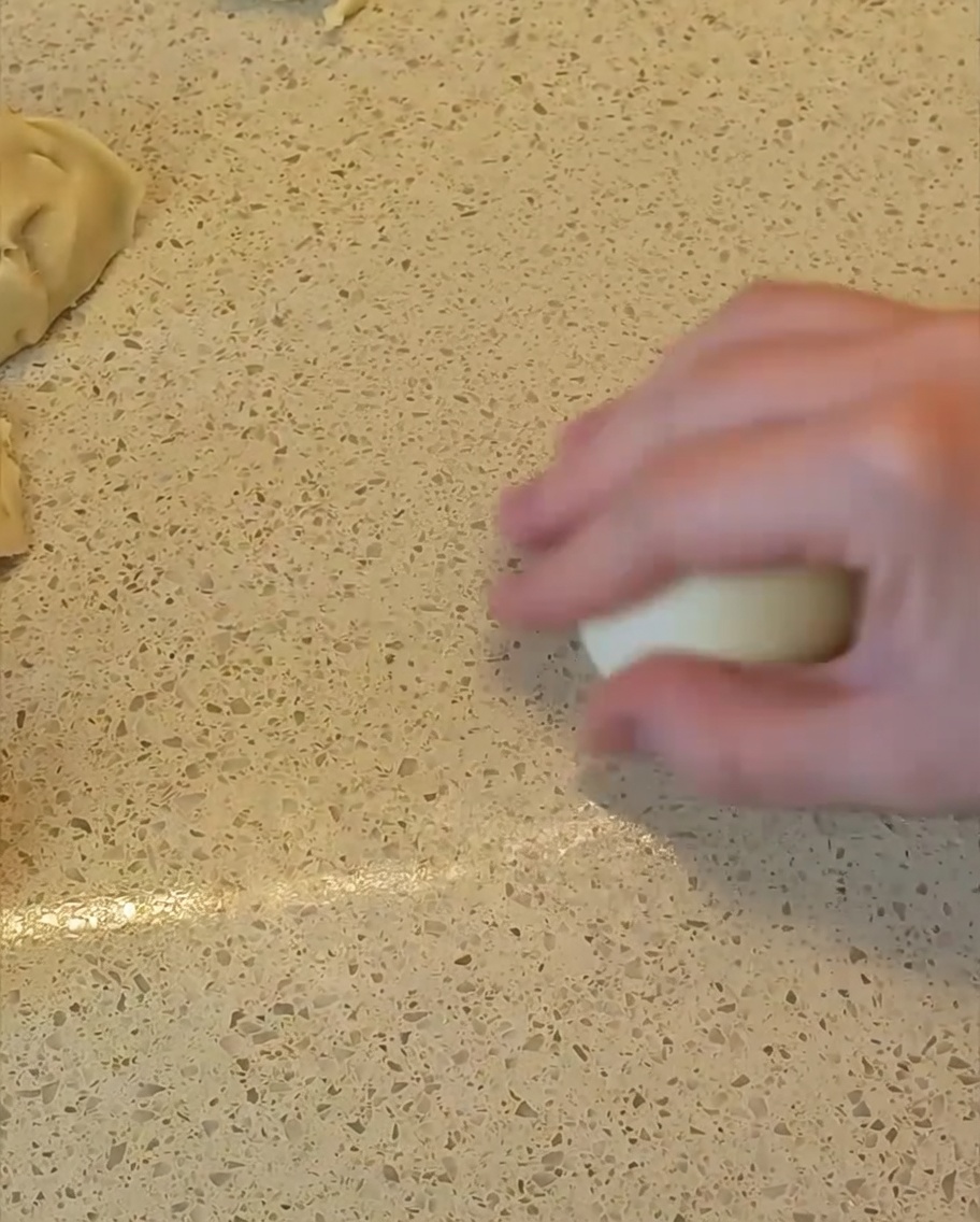 Dłoń rolująca kawałek ciasta na blacie, aby uformować z niego gładką, okrągłą kulkę.