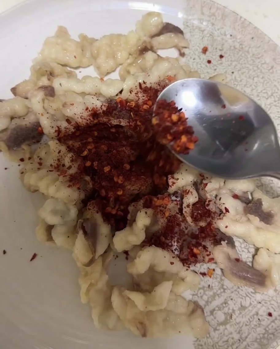 Łyżka nasypująca chili w proszku i kmin rzymski na zblanszowane kawałki tłuszczu wołowego na talerzu.