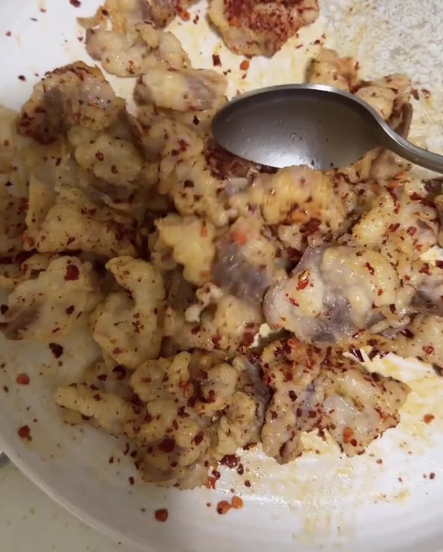 Łyżka mieszająca kawałki tłuszczu wołowego z chili w proszku i kminem rzymskim w celu ich równomiernego pokrycia.