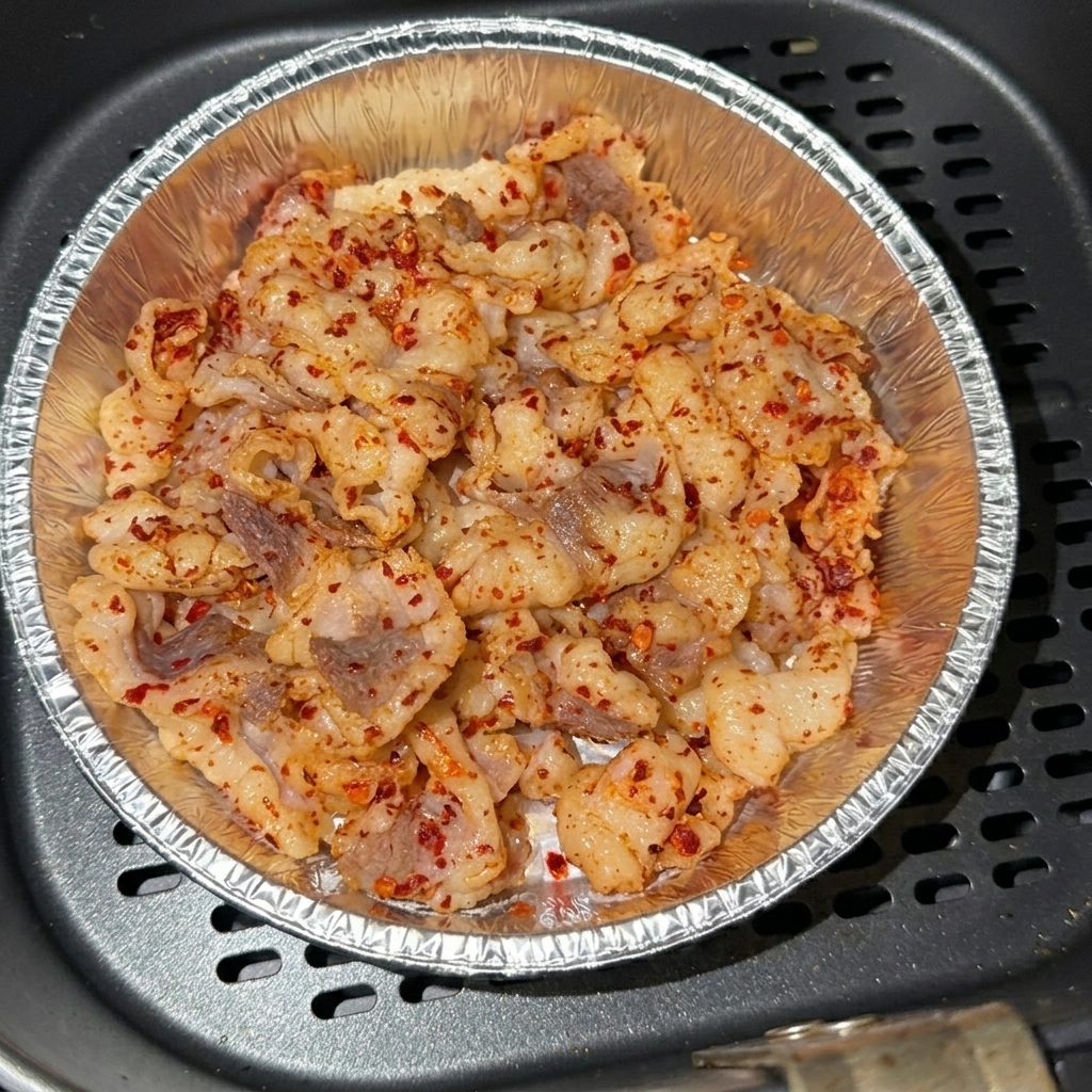 Przyprawione plastry tłuszczu wołowego ułożone w aluminiowej foremce wewnątrz kosza frytkownicy beztłuszczowej.
