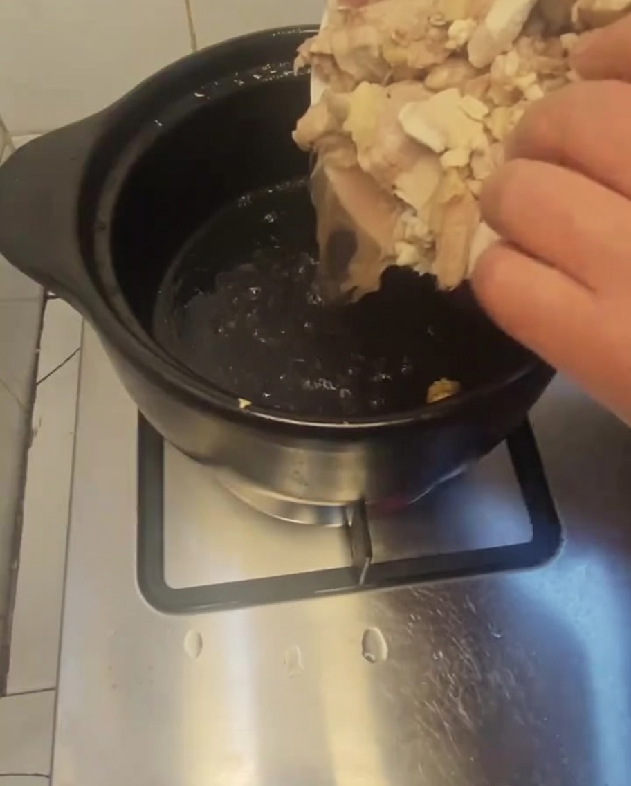 Zblanszowane kawałki kurczaka przekładane z białego talerza do ciemnego, rozgrzanego glinianego garnka.