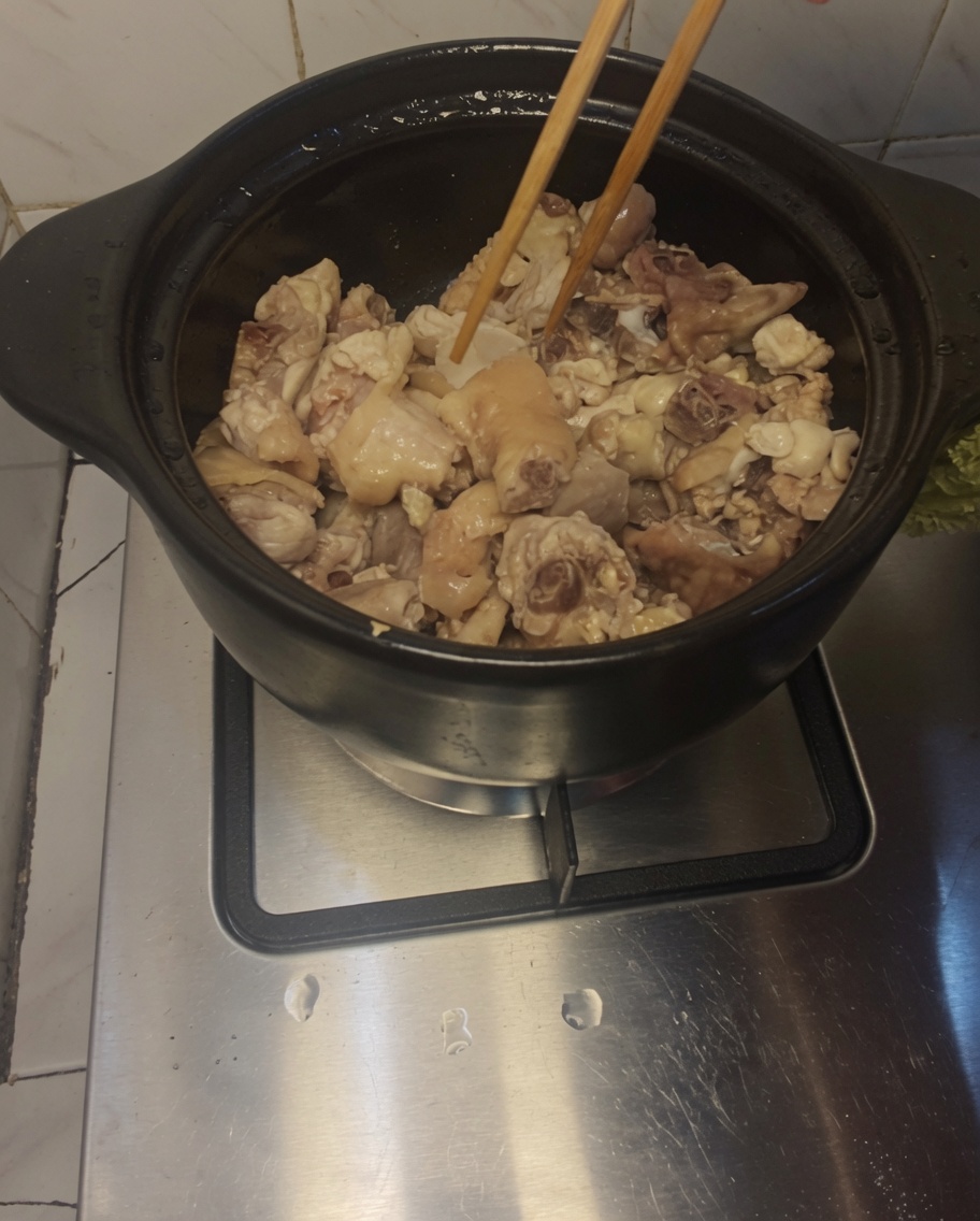 Drewniane pałeczki mieszające kawałki kurczaka i plastry imbiru w rozgrzanym glinianym garnku.