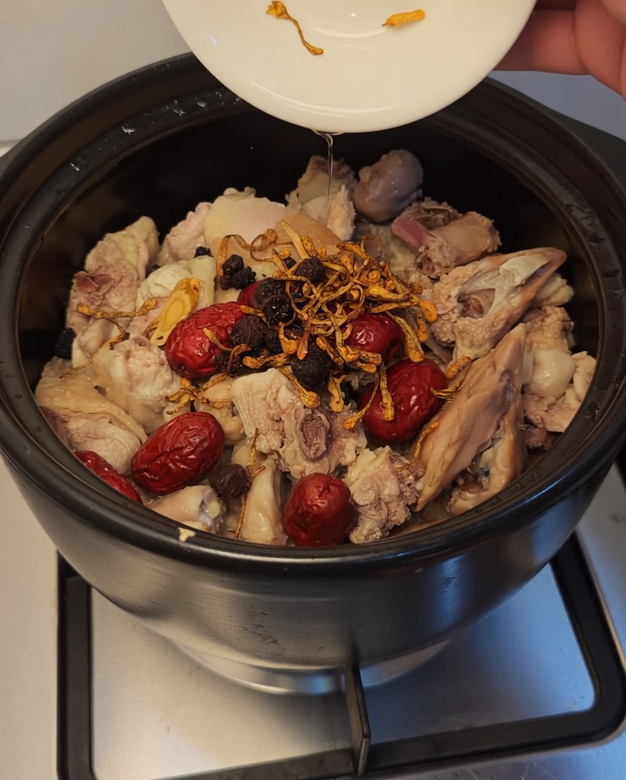 Kwiaty kordycepsu, ciemne jagody goji i longan dodawane do kurczaka i daktyli w garnku.