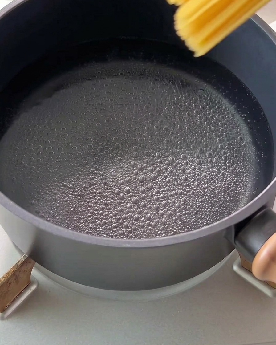 Surowy makaron spaghetti wrzucany do garnka z wrzącą wodą.