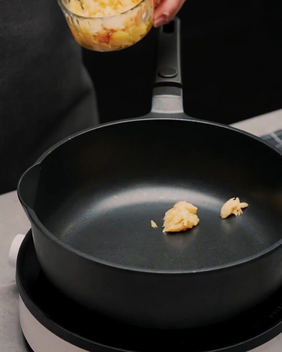 Czarna patelnia z porcjami pasty czosnkowej mieszanymi z oliwą i suszonymi płatkami chili.