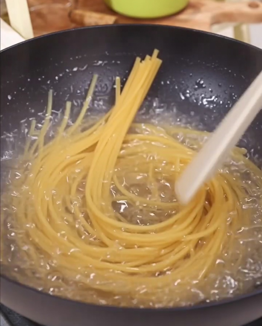 Nitki spaghetti zanurzane w garnku z gotującą się wodą.