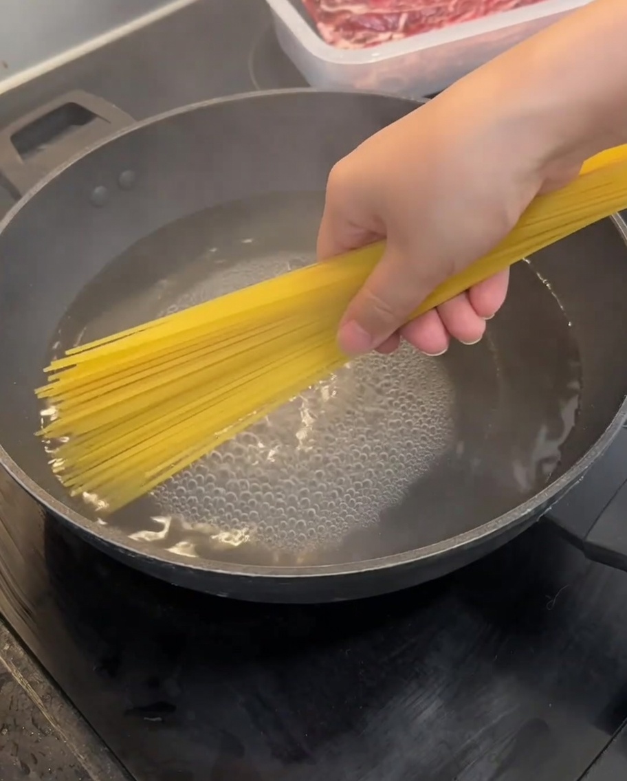 Surowy makaron spaghetti zanurzany we wrzącej wodzie w woku.