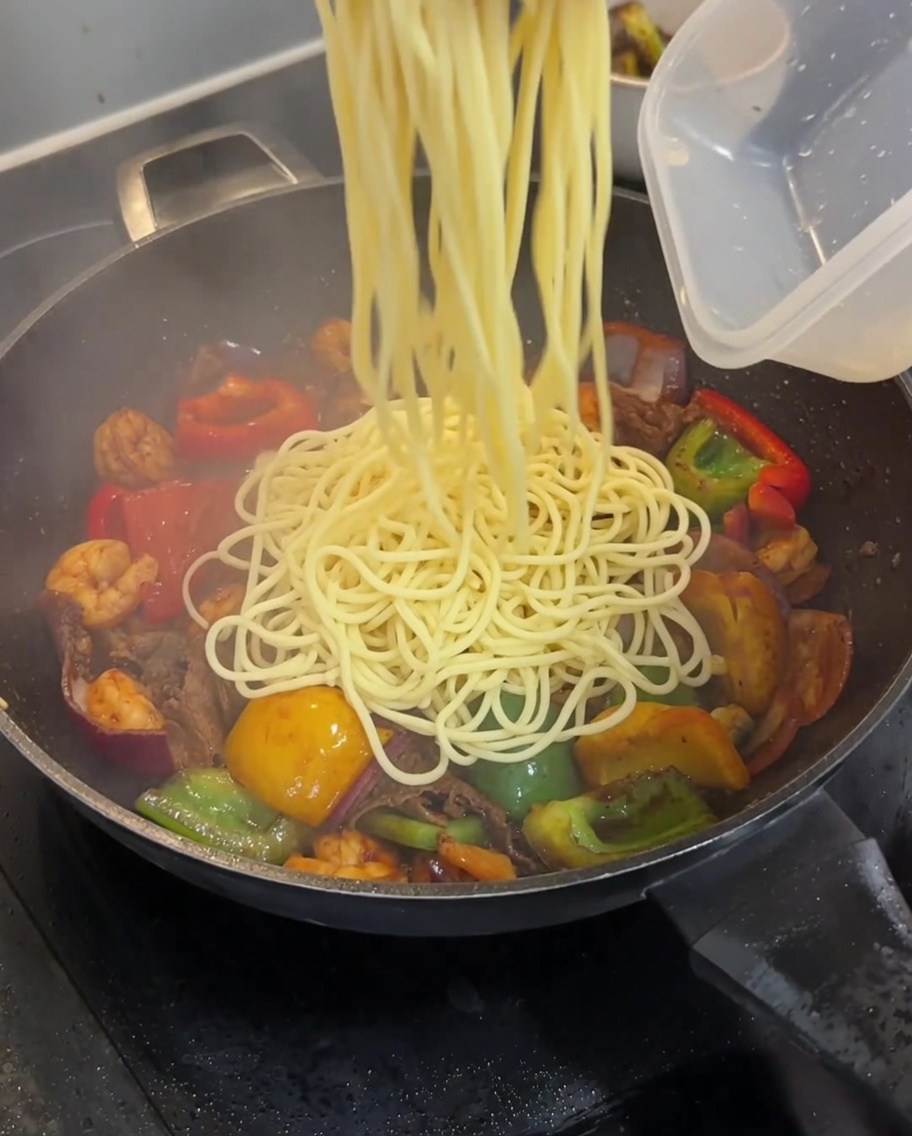 Ugotowane spaghetti dodawane do woka z mięsem i warzywami.