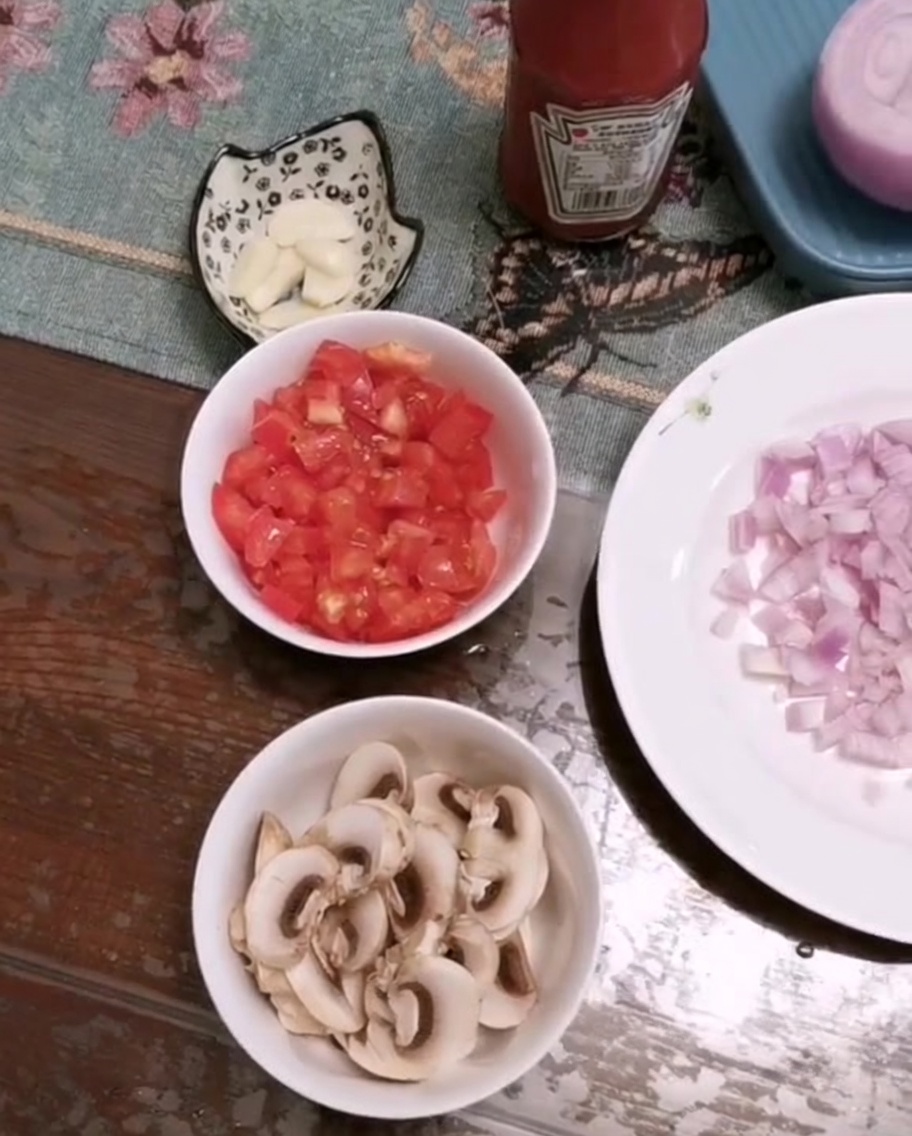 Miska z posiekanymi pomidorami, plastrami pieczarek i posiekanym czosnkiem na stole.