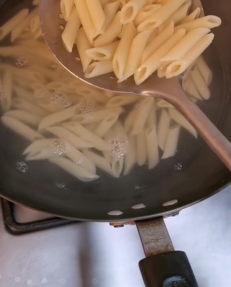 Makaron penne wyjmowany z wrzącej wody za pomocą dużej łyżki cedzakowej.