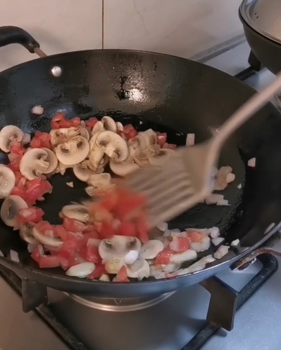 Mieszanie ugotowanego penne i pasków wołowiny w woku z podsmażonymi warzywami.