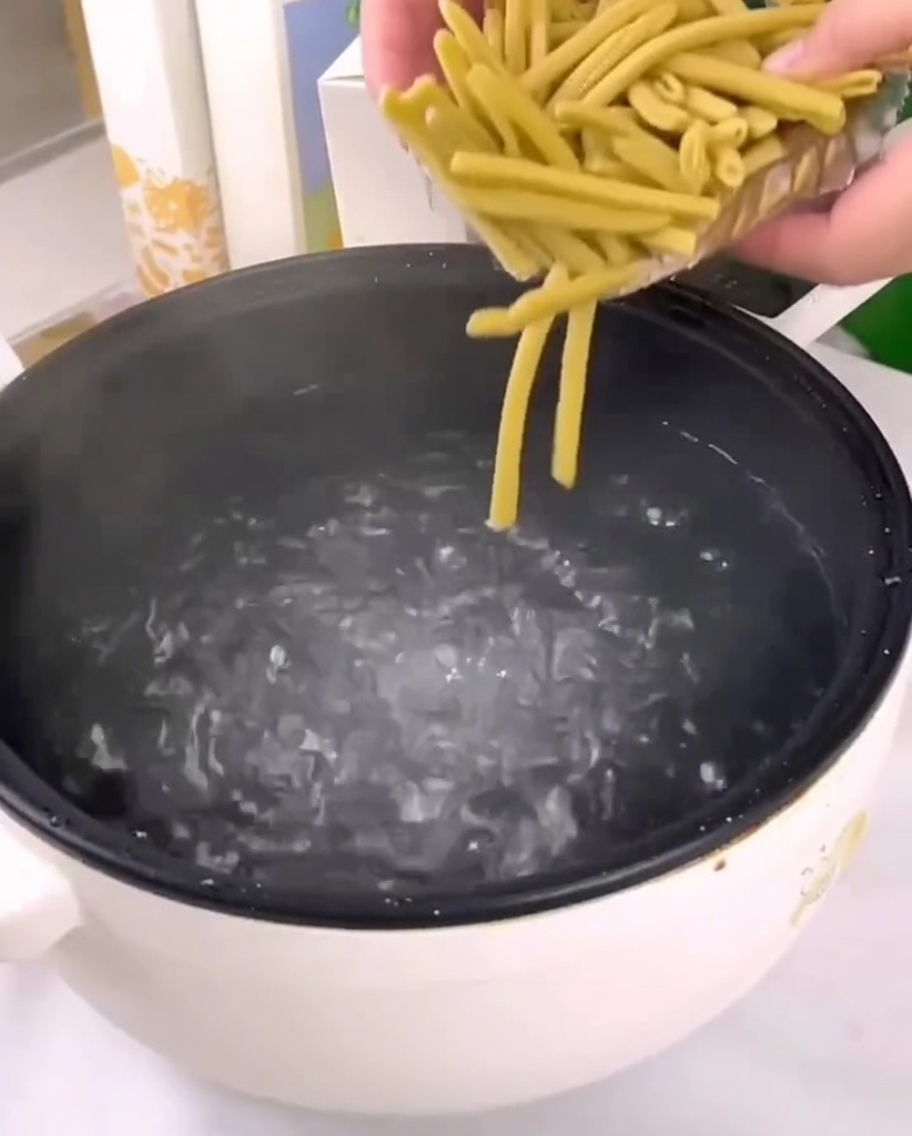 Suszony makaron penne z prosa wsypywany do garnka z wrzącą wodą.