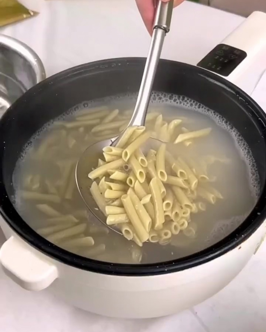 Ugotowany makaron penne przekładany z garnka do miski z zimną wodą za pomocą łyżki cedzakowej.