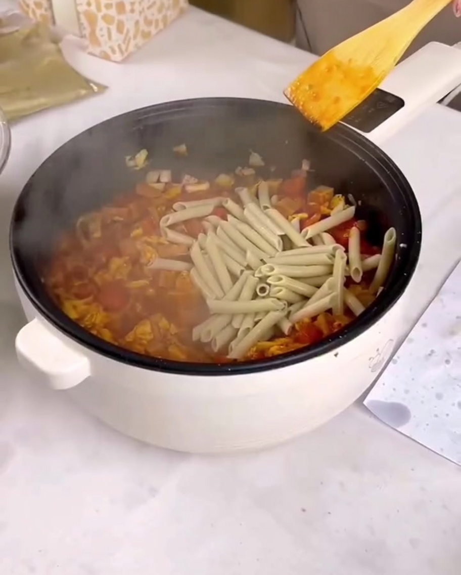 Ugotowany makaron penne dodawany na patelnię z sosem i podsmażonymi składnikami.