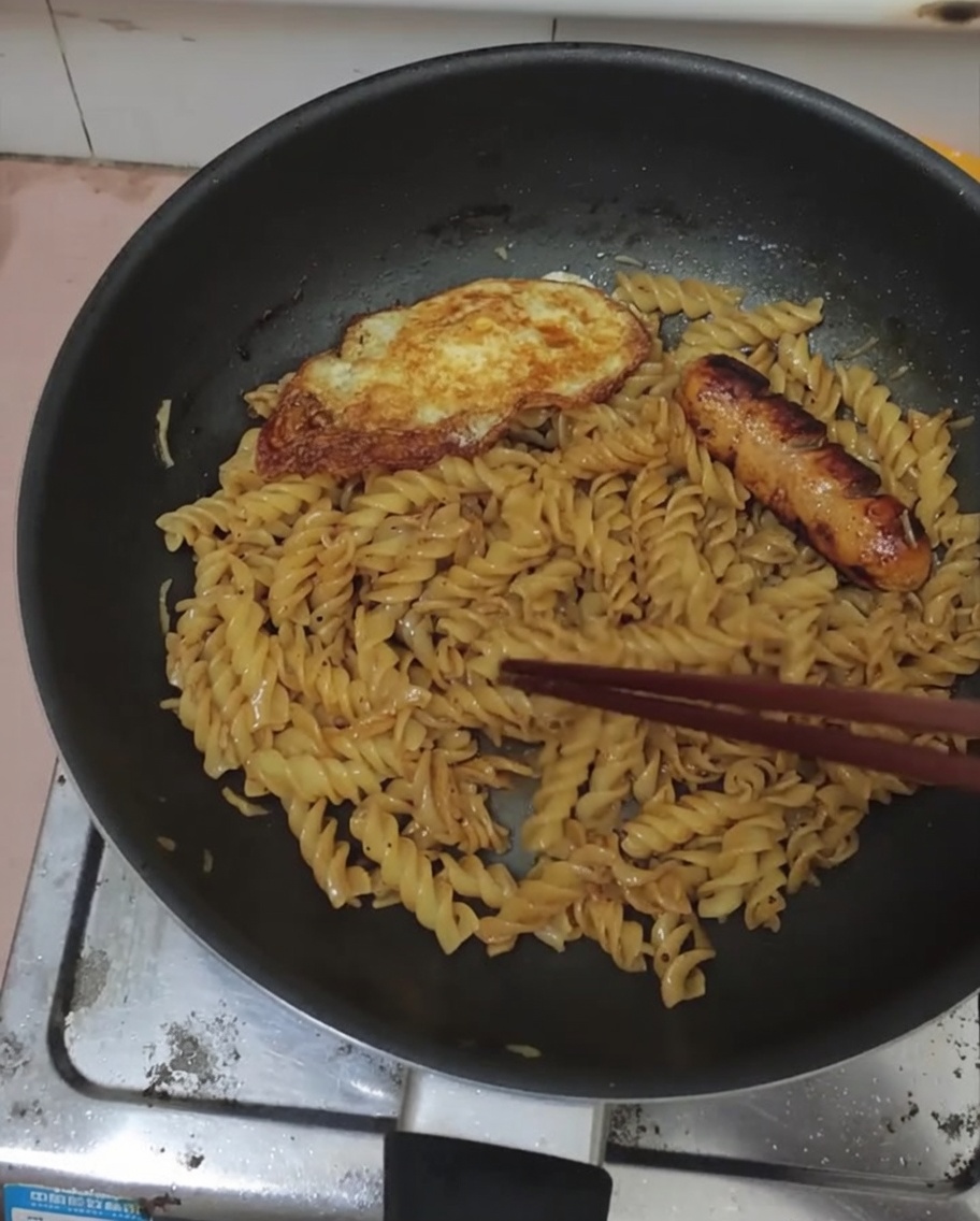 Jajko sadzone i kiełbasa ułożone na wierzchu makaronu z sosem.