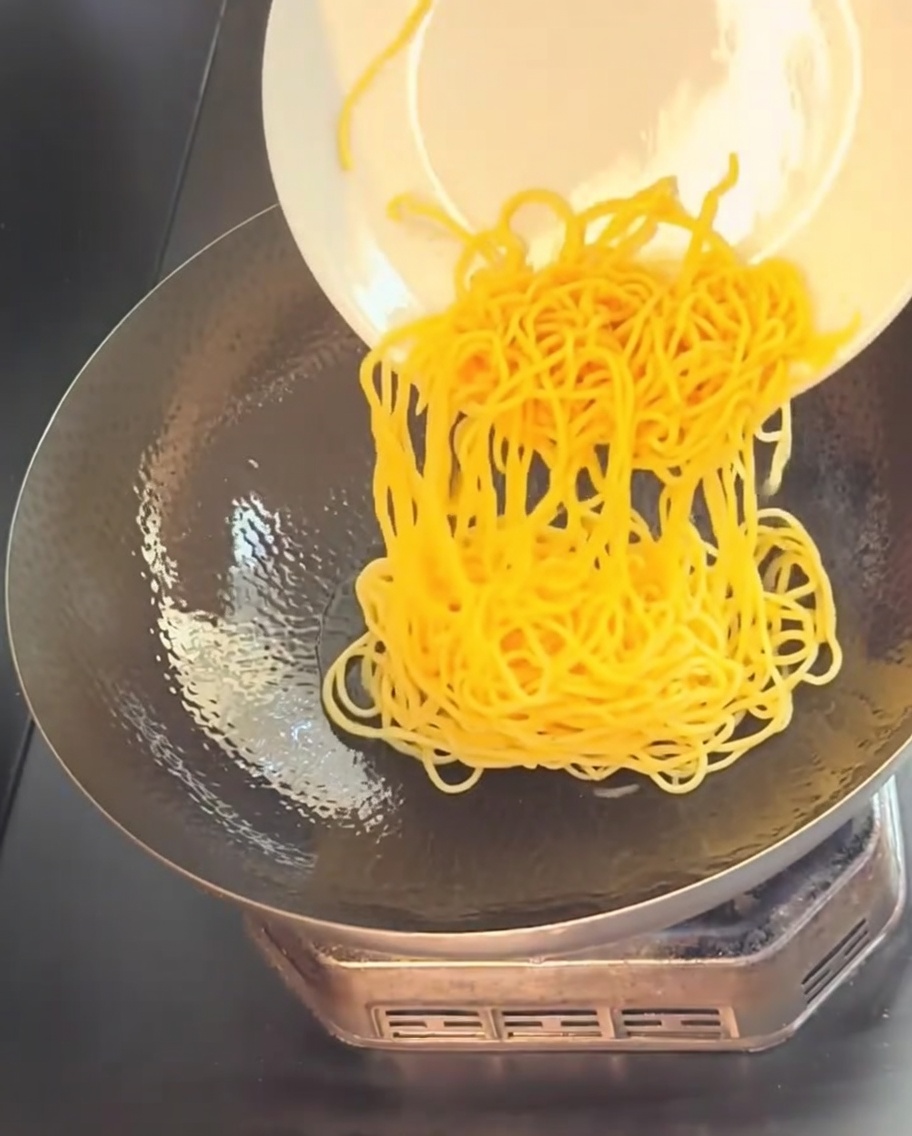 Ugotowany makaron spaghetti zsuwany z białego talerza do gorącego woka z olejem.