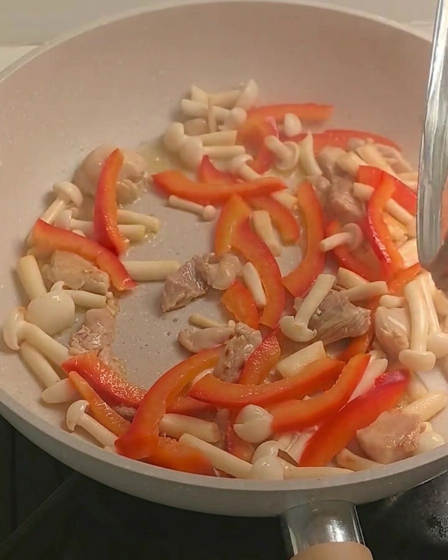 Ugotowany makaron fusilli dodawany do patelni z kurczakiem i kolorowymi warzywami.