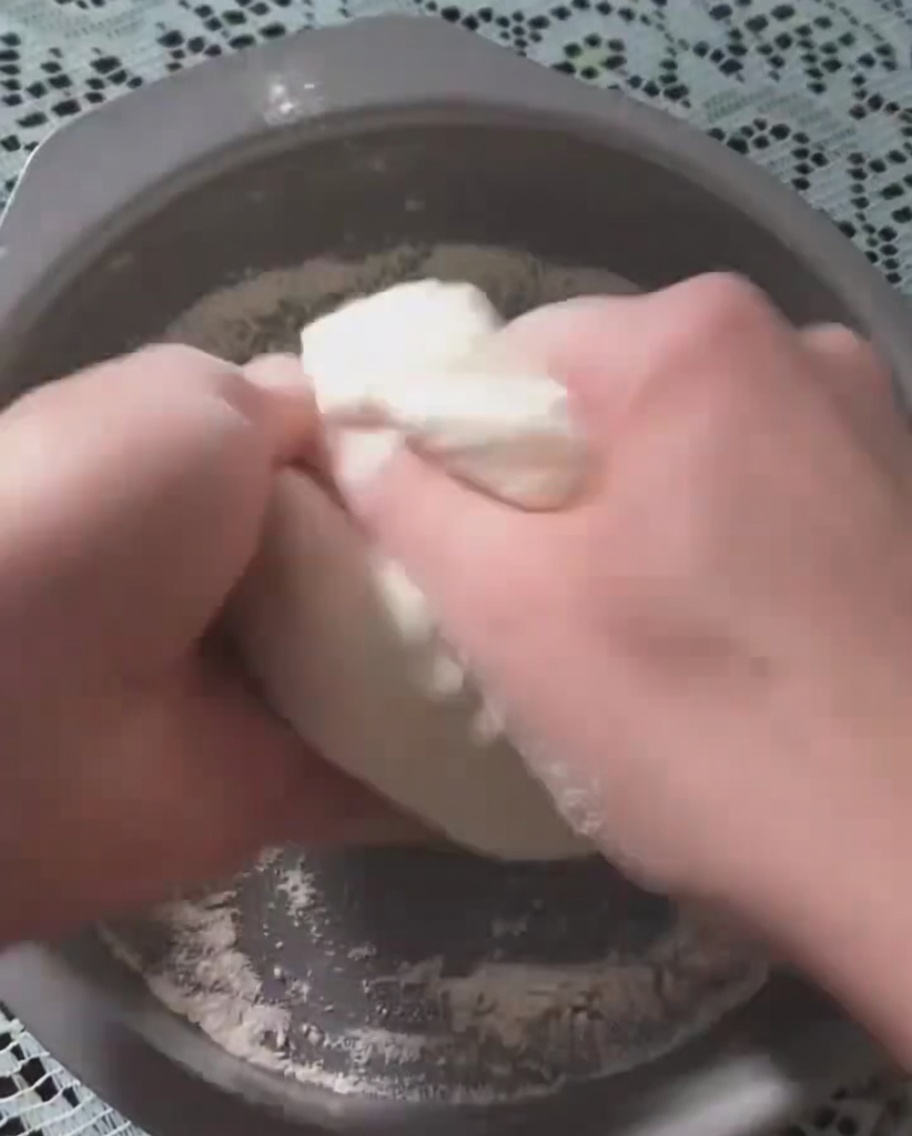 Dłonie rozciągające wyrośnięte ciasto w okrągłej formie do pieczenia.