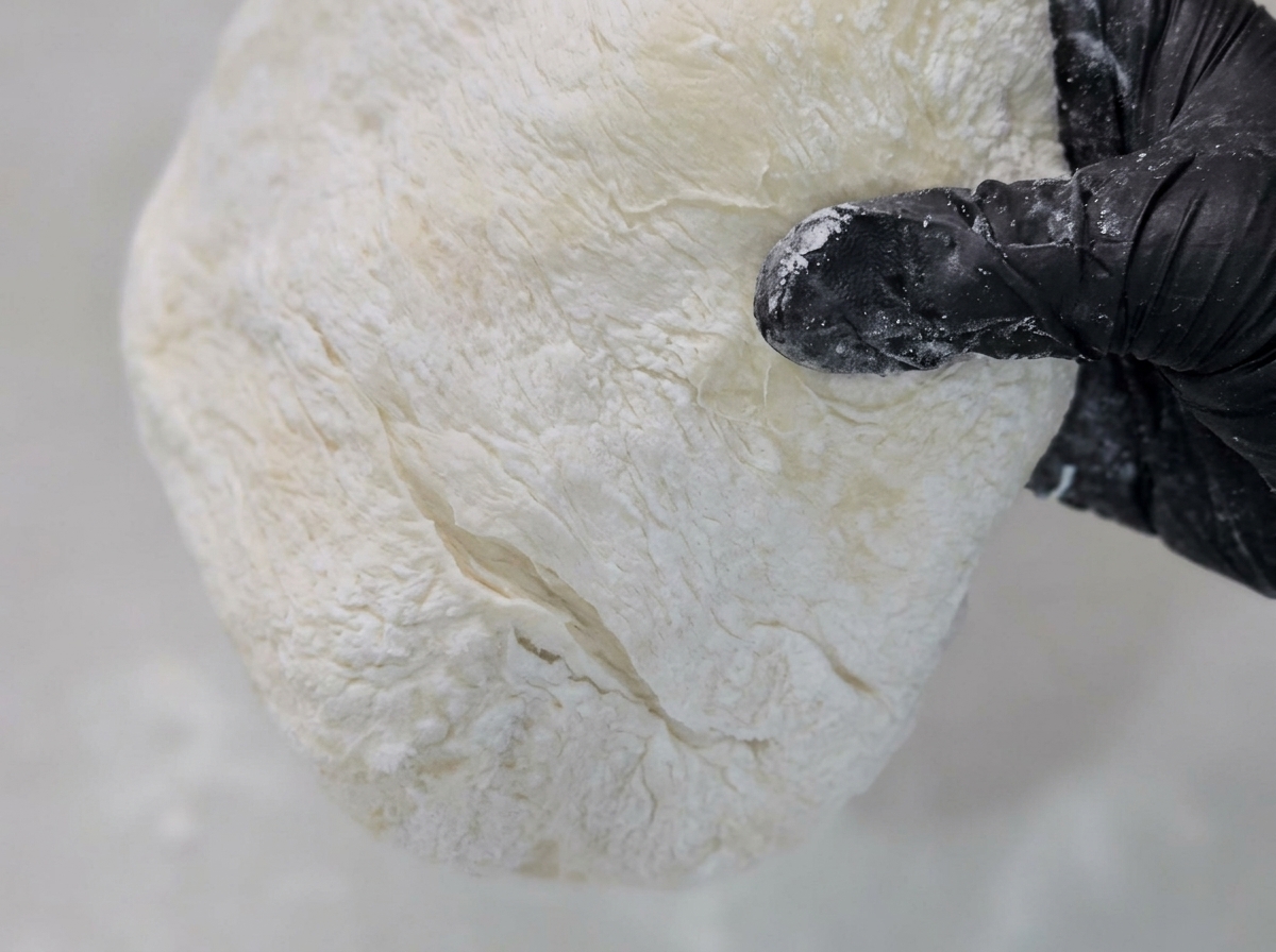 Ciasto na pizzę rozciągane na powierzchni posypanej kaszą kukurydzianą.