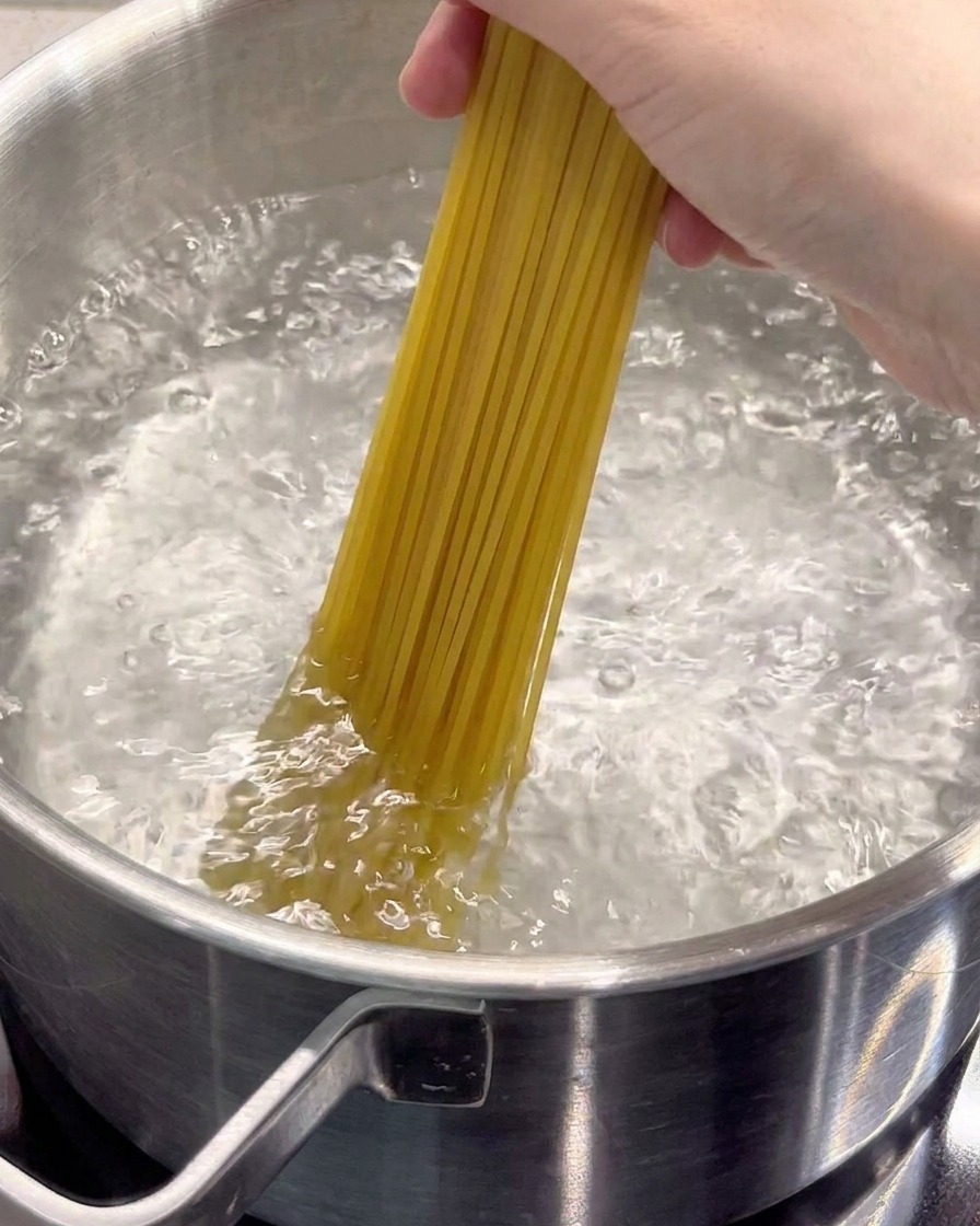 Surowy makaron spaghetti wkładany do garnka z wrzącą, osoloną wodą.