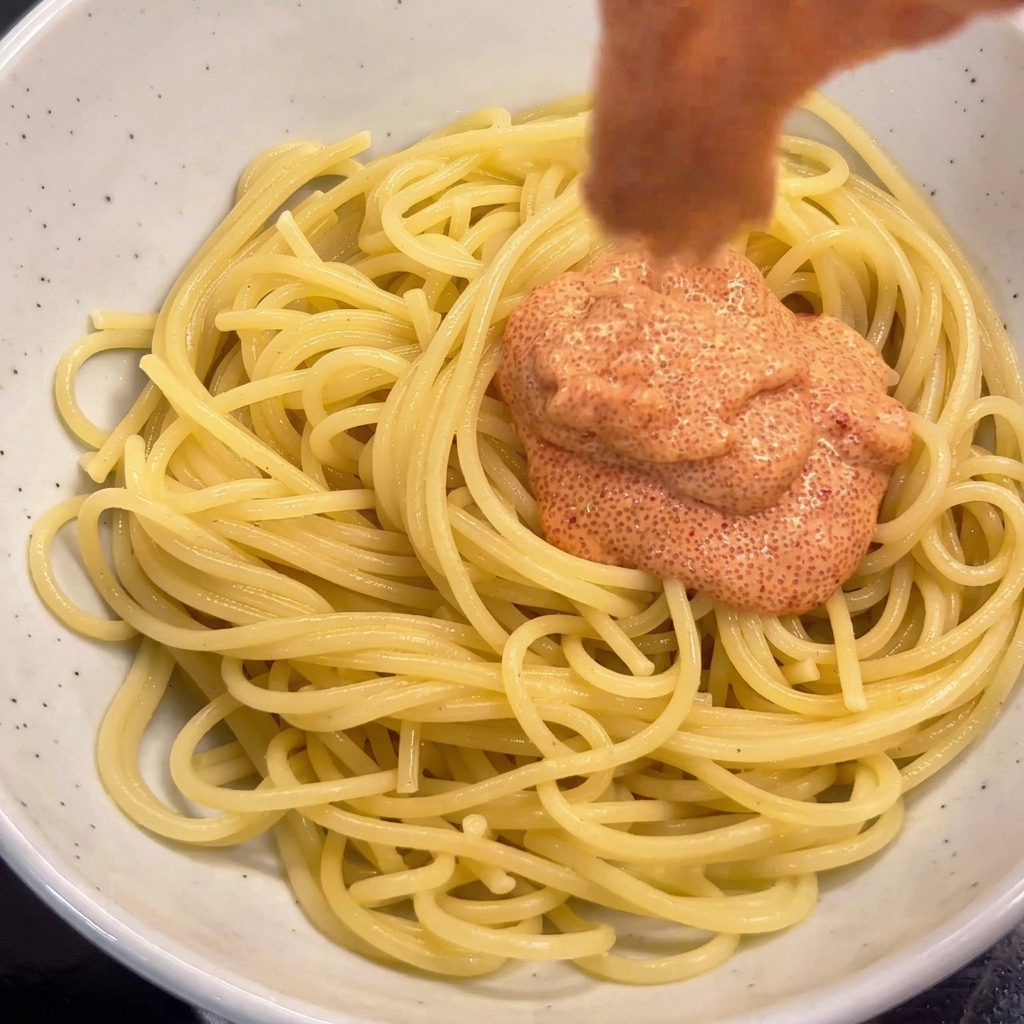 Dodawanie sosu mentaiko do spaghetti w misce i mieszanie pałeczkami.