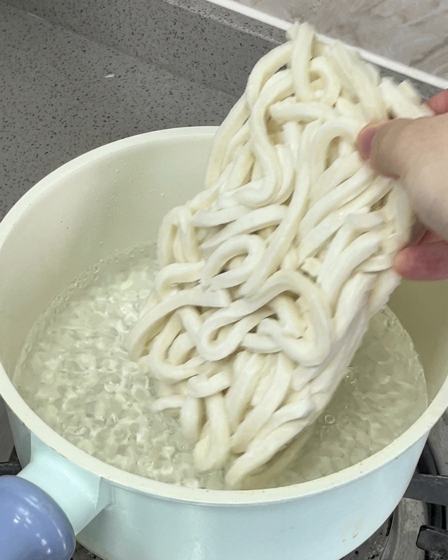 Kluski udon zanurzane w garnku z wrzącą wodą.