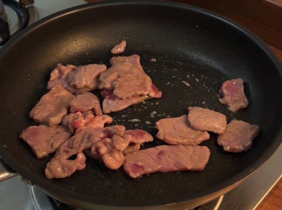 Pokrojona czerwona cebula dodana do patelni z usmażoną wołowiną, mieszane nad ogniem.