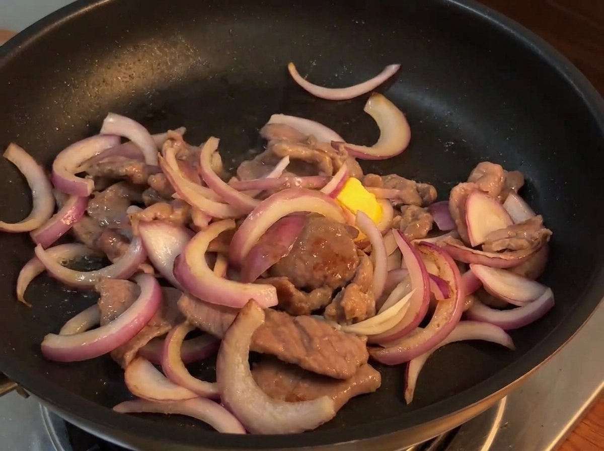 Sos do stir-fry wylewany z małej miseczki na mieszankę wołowiny z cebulą na gorącej patelni.