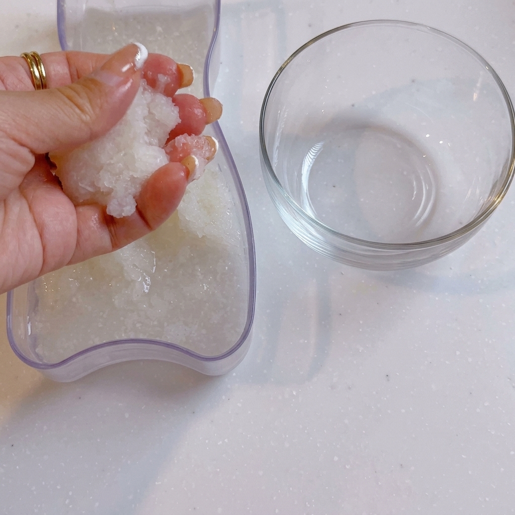 Dłoń odciskająca wodę ze startej rzodkwi daikon obok przezroczystej szklanej miski.