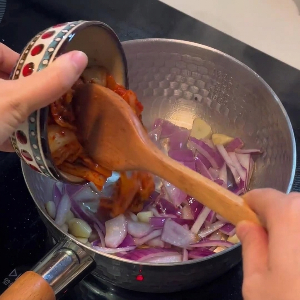 Kimchi dodawane do garnka i mieszane z podsmażoną cebulą.