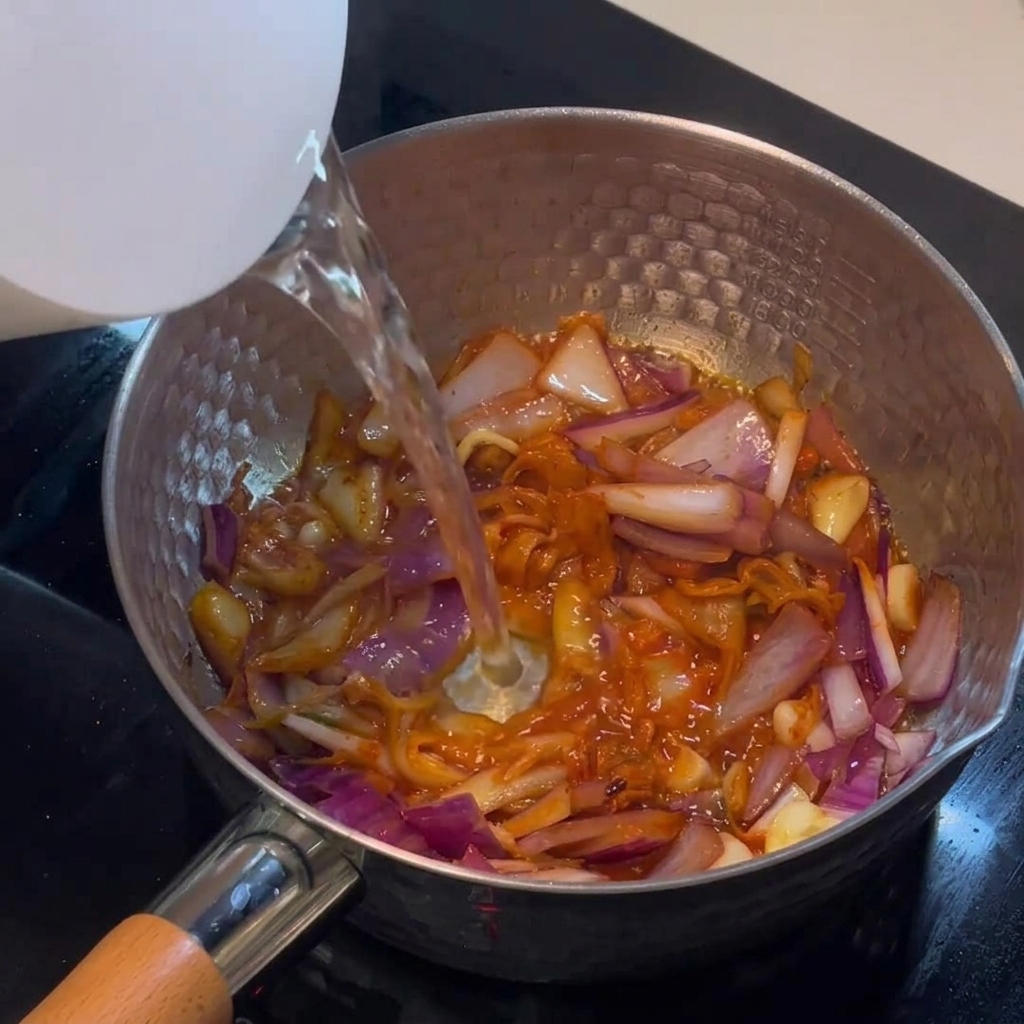Gorąca woda wlewana z czajnika do garnka z kimchi i cebulą.