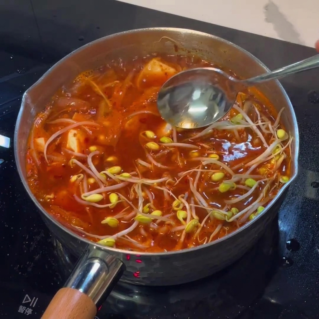 Łyżka gęstej czerwonej pasty gochujang mieszana z bulgoczącym gulaszem.