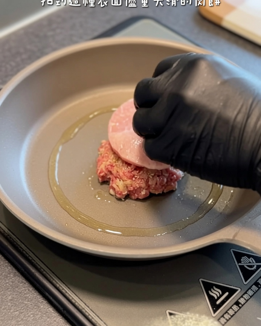 Surowy kotlet hamburgerowy układany na gorącej patelni z oliwą za pomocą łopatki.