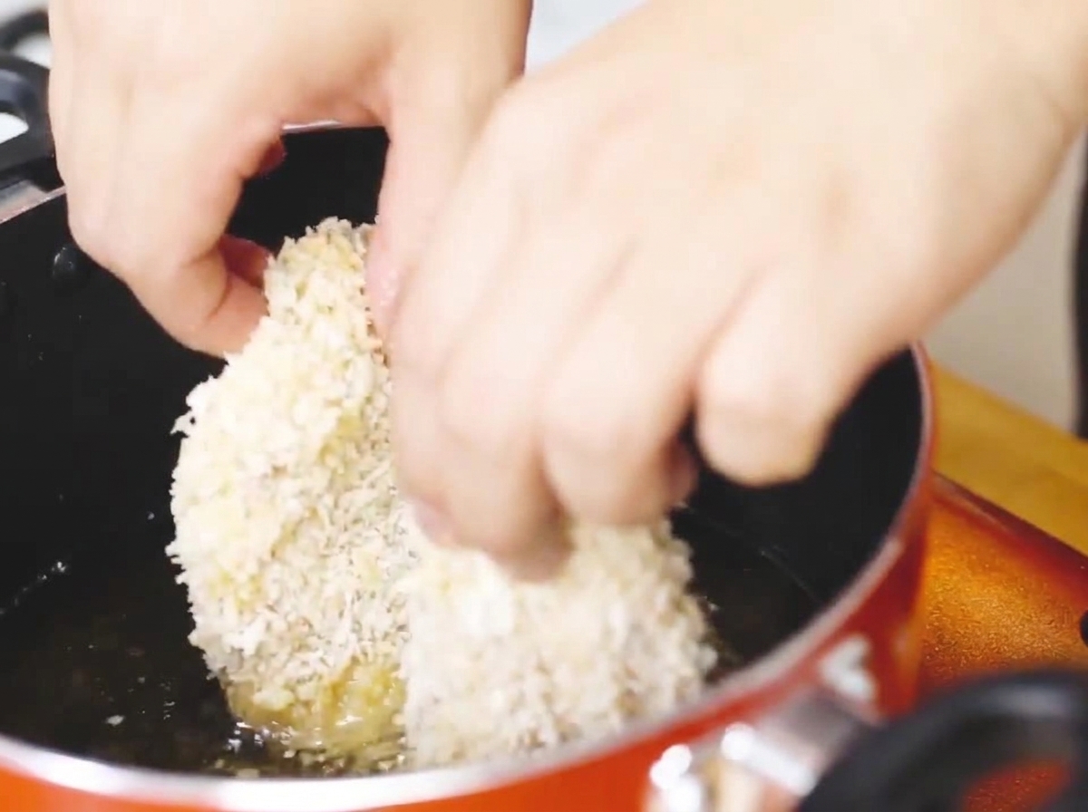 Panierowany kotlet z kurczaka smażący się na patelni z gorącym olejem na złoty kolor.