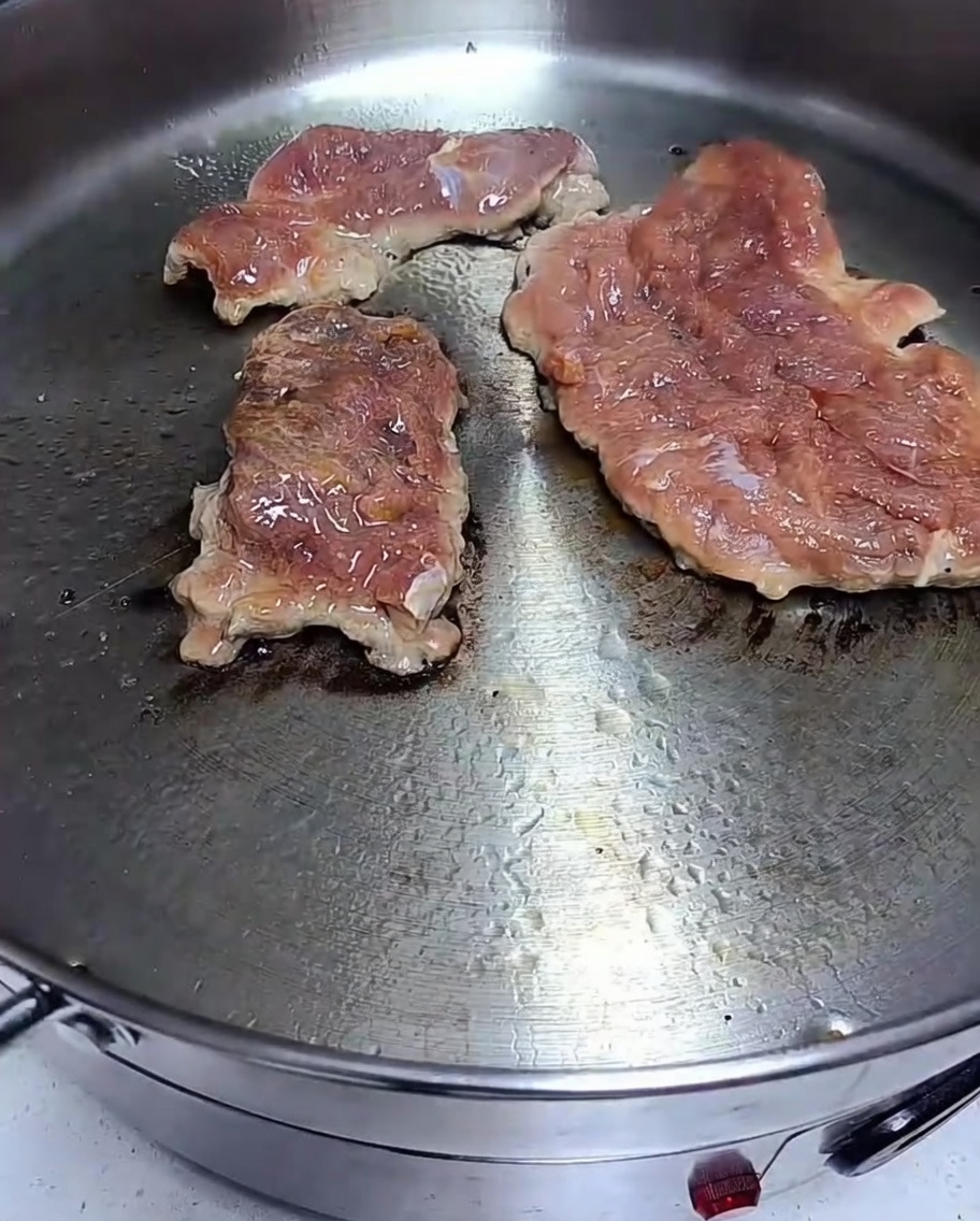 Marynowany kotlet wieprzowy smażący się na gorącej patelni z widocznym zrumienieniem na powierzchni.