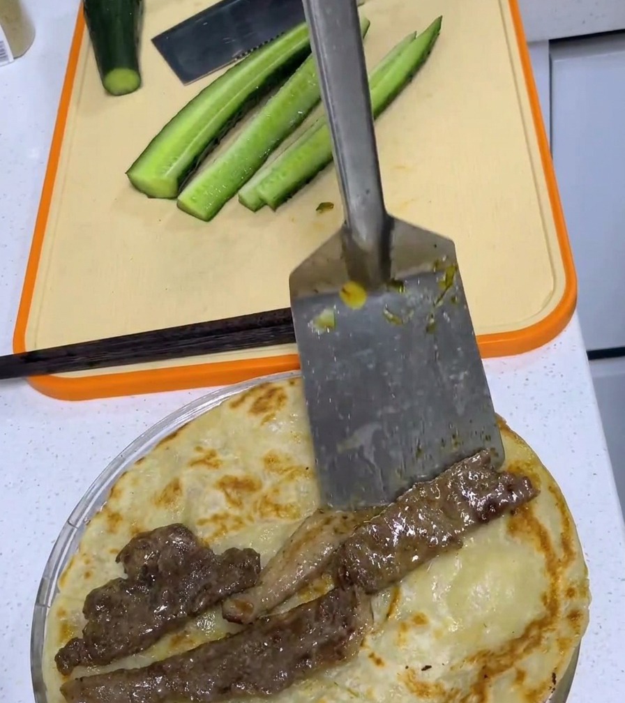 Smażony kotlet wieprzowy umieszczony na środku złotobrązowego placka scallion na desce do krojenia.