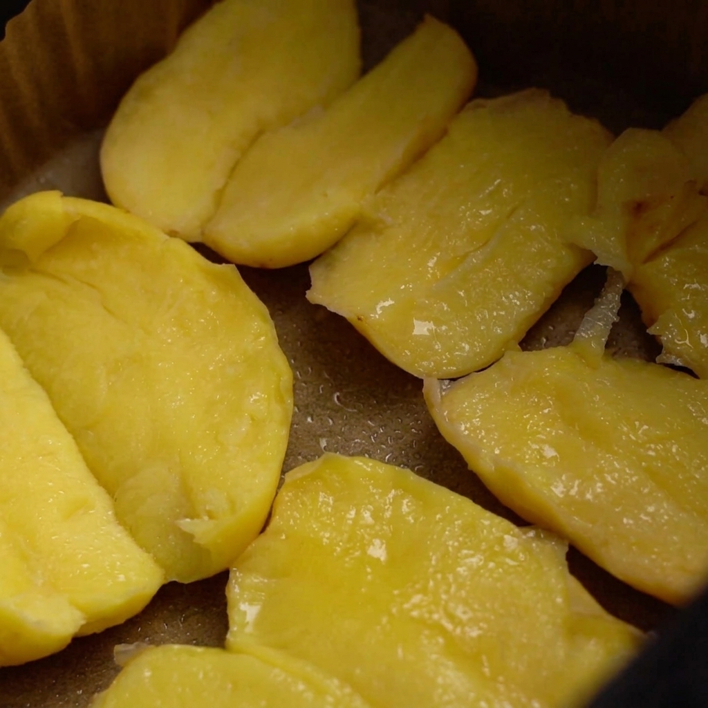 Ziemniaki w koszu frytkownicy pokryte olejem, przyprawiane grubą solą i posypką z nasion sezamu.