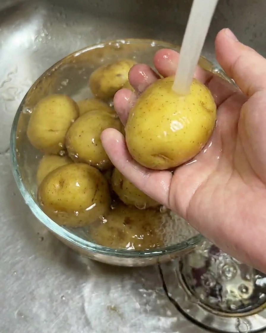 Młode ziemniaki myte w szklanej misce pod bieżącą wodą.