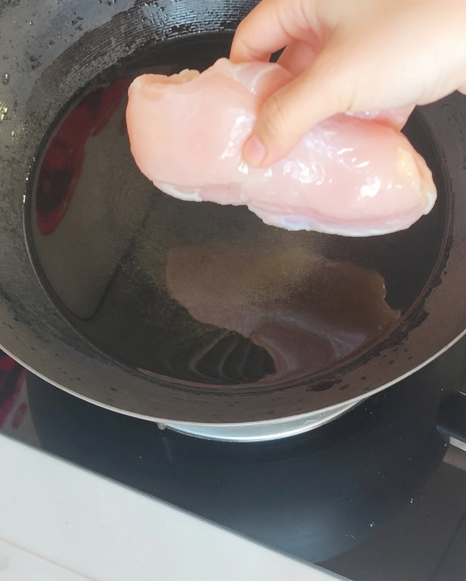 Pierś z kurczaka zanurzona we wrzącej wodzie w woku wraz z aromatycznym imbirem i zieloną cebulką.