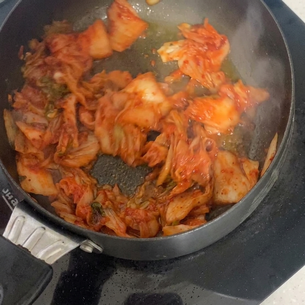 Kawałki kwaśnego kimchi skwierczące i mieszane na gorącej patelni z olejem.