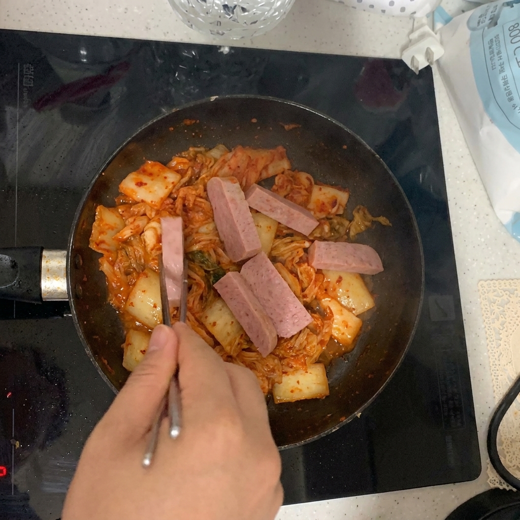 Plastry mielonki z puszki dodawane na patelnię obok smażącego się kimchi.