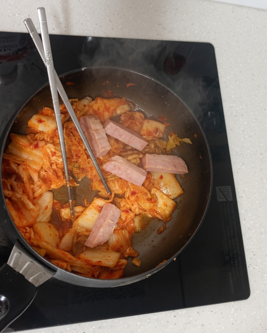 Woda wlewana z miski na patelnię z podsmażonym kimchi i mielonką.
